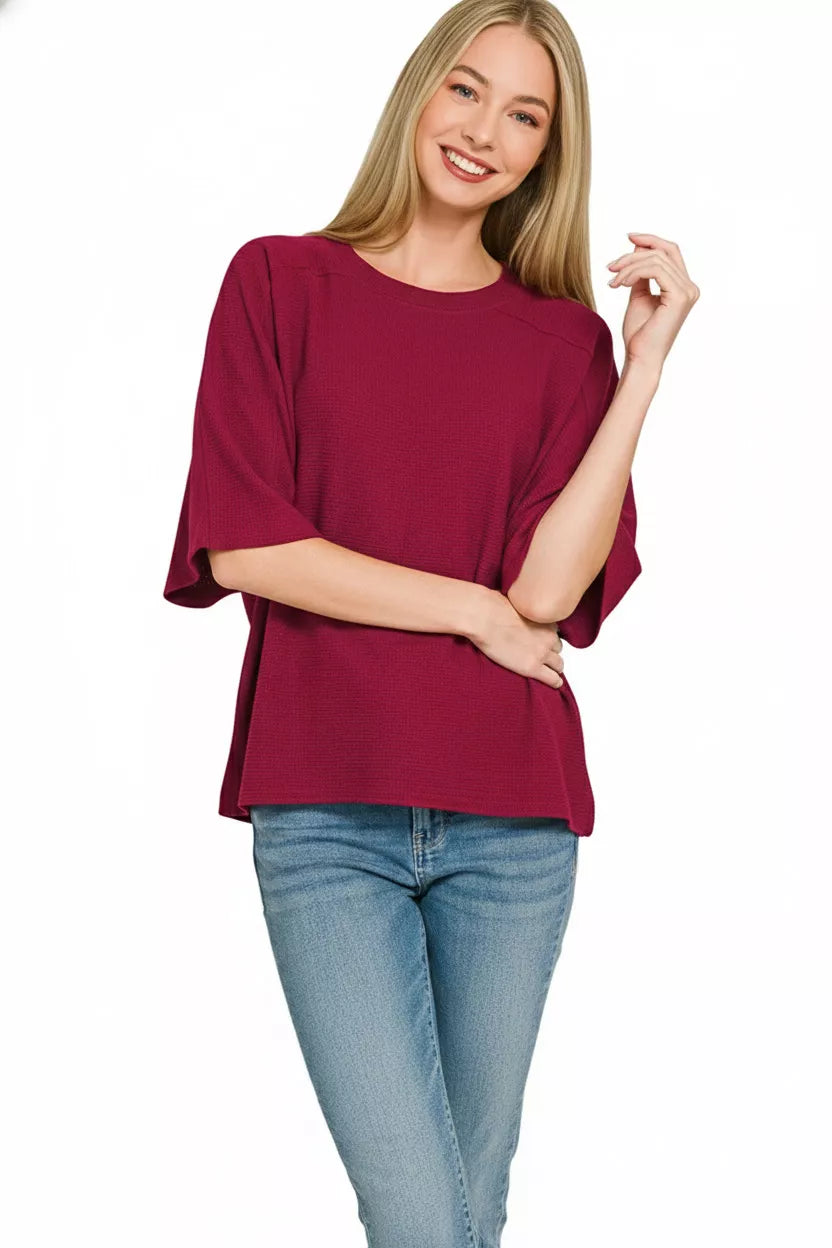 A woman models a burgundy Zenana double knit short sleeve top paired with blue jeans.