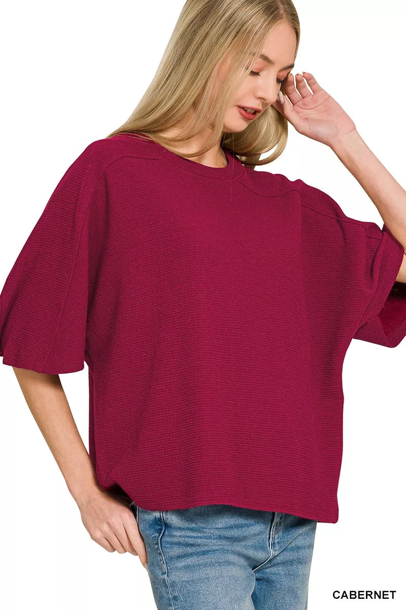 A woman wears a cabernet-colored Zenana double knit short sleeve top with blue jeans.